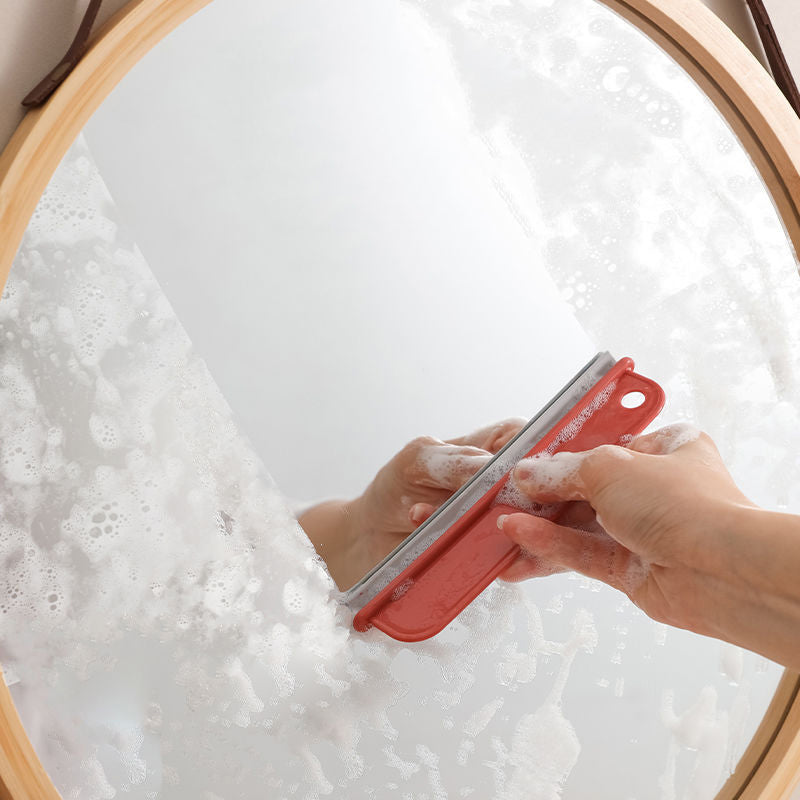 a hand with a red tool cleaning a mirror